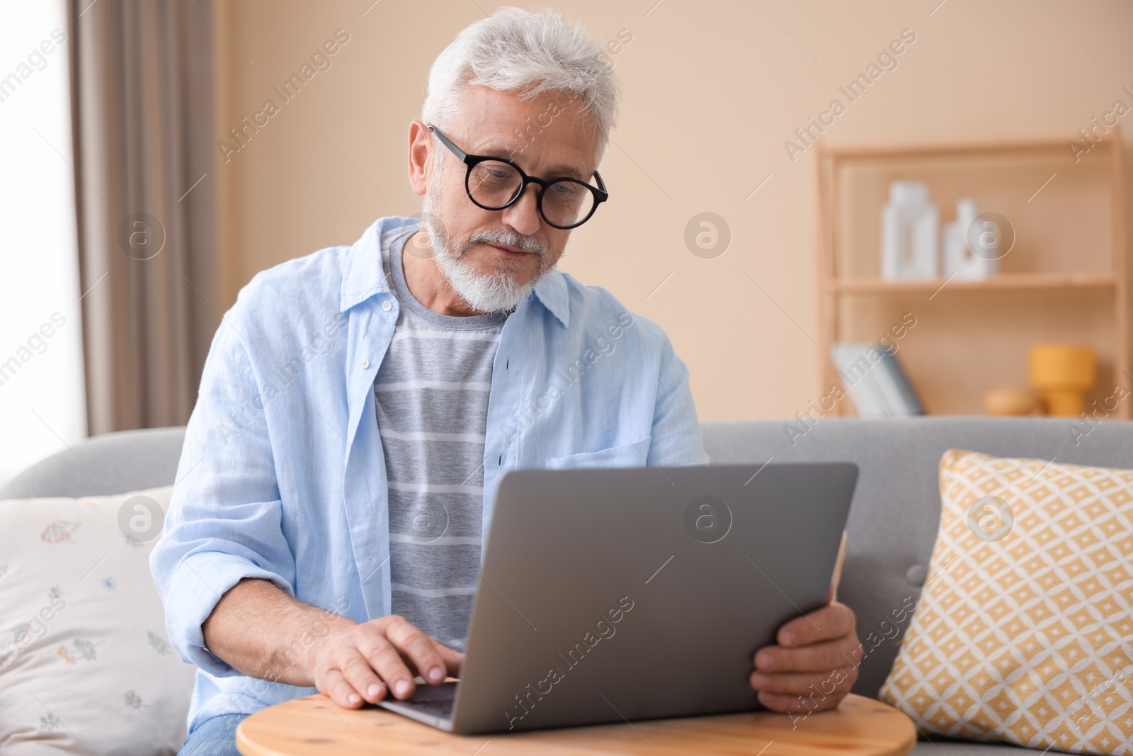 Photo of Senior man using laptop at wooden table indoors