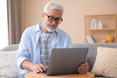 Photo of Senior man using laptop at wooden table indoors