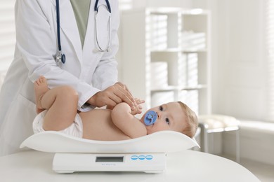 Pediatrician weighting little child in clinic, closeup. Checking baby's health