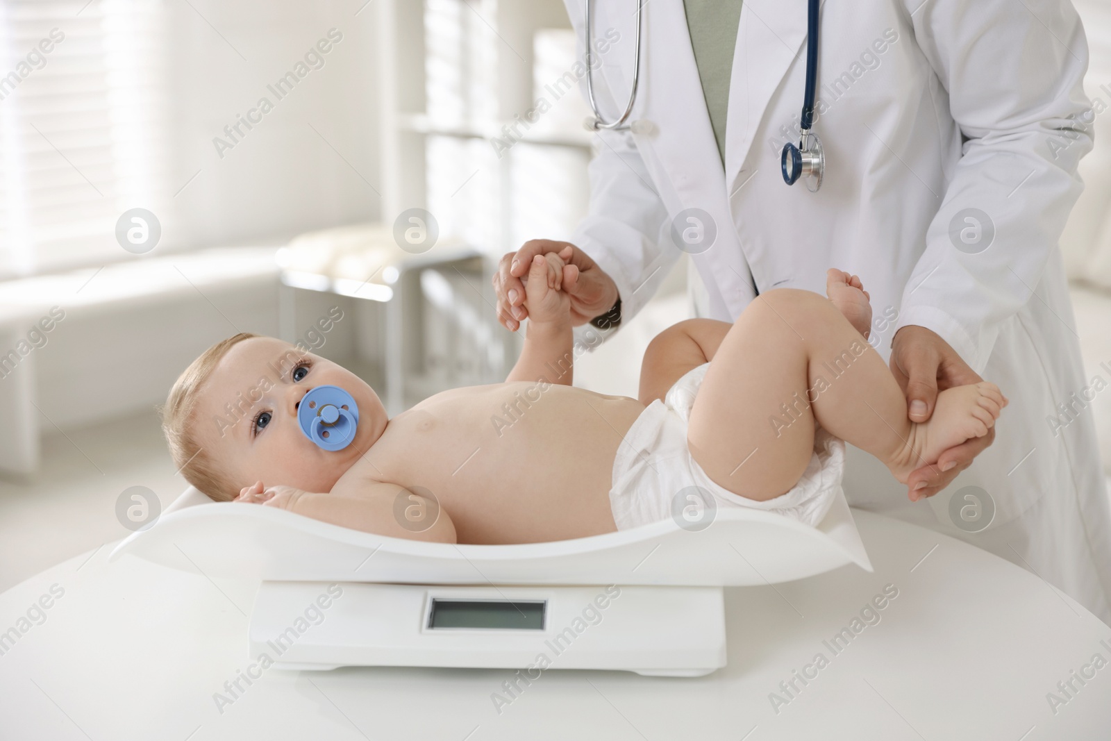 Photo of Pediatrician weighting little child in clinic, closeup. Checking baby's health