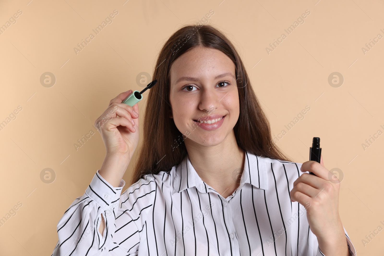 Photo of Smiling teenage girl applying mascara on beige background