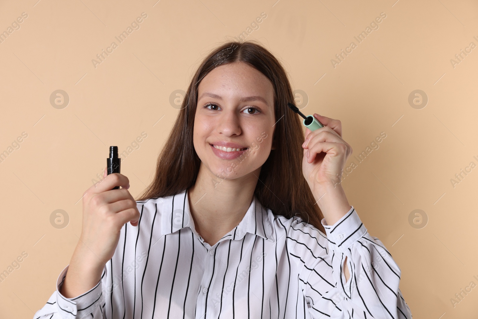 Photo of Smiling teenage girl applying mascara on beige background