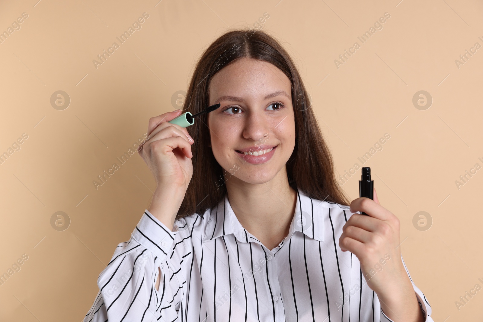 Photo of Smiling teenage girl applying mascara on beige background