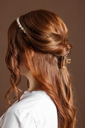 Photo of Teenage girl with stylish hair accessories on brown background, back view