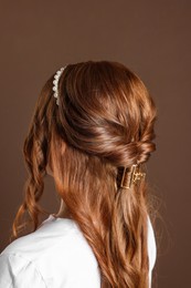 Photo of Teenage girl with stylish hair accessories on brown background, back view