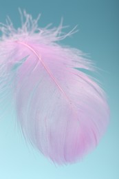 Photo of Fluffy pink feather on light blue background, closeup