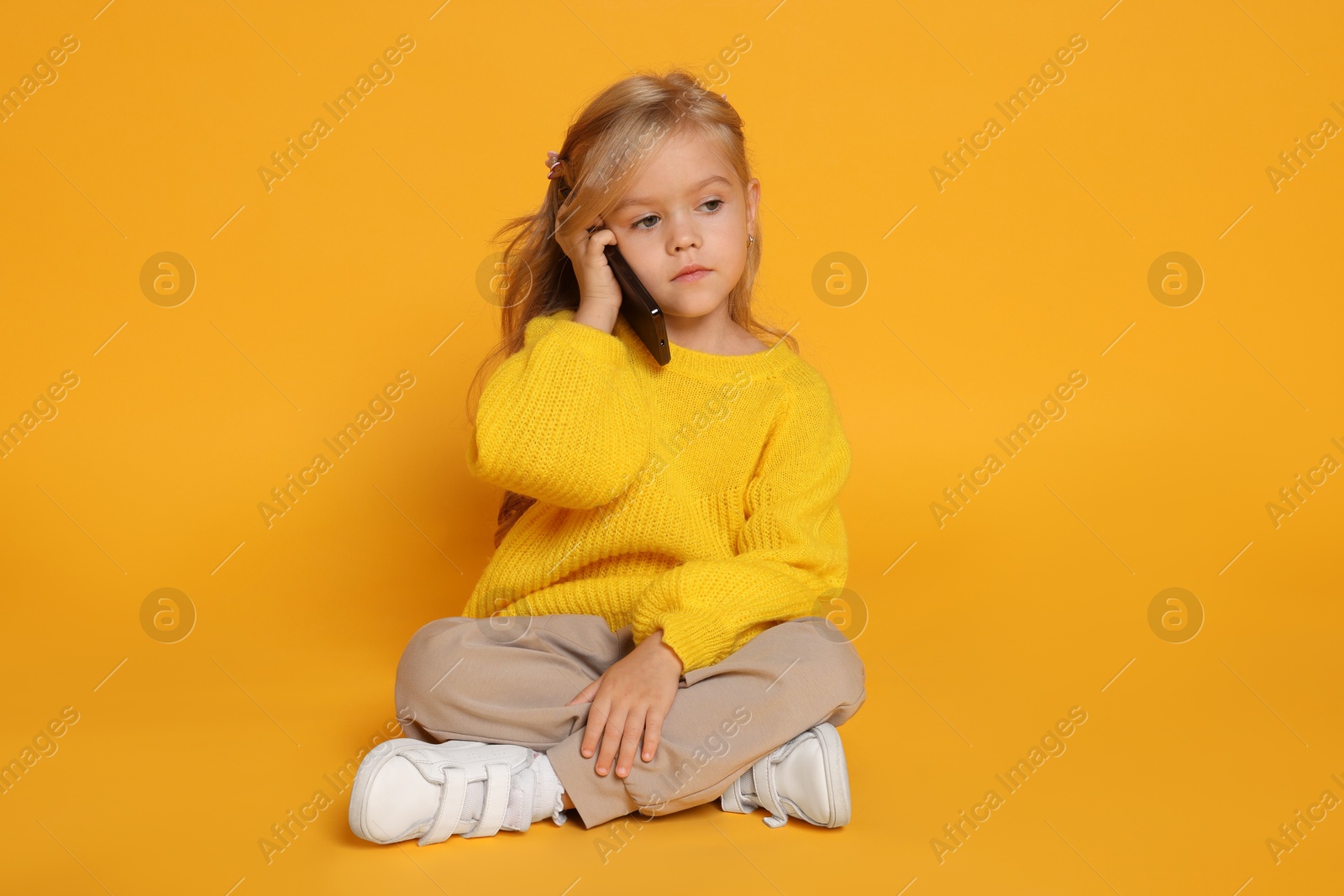 Photo of Cute little girl talking on smartphone against orange background