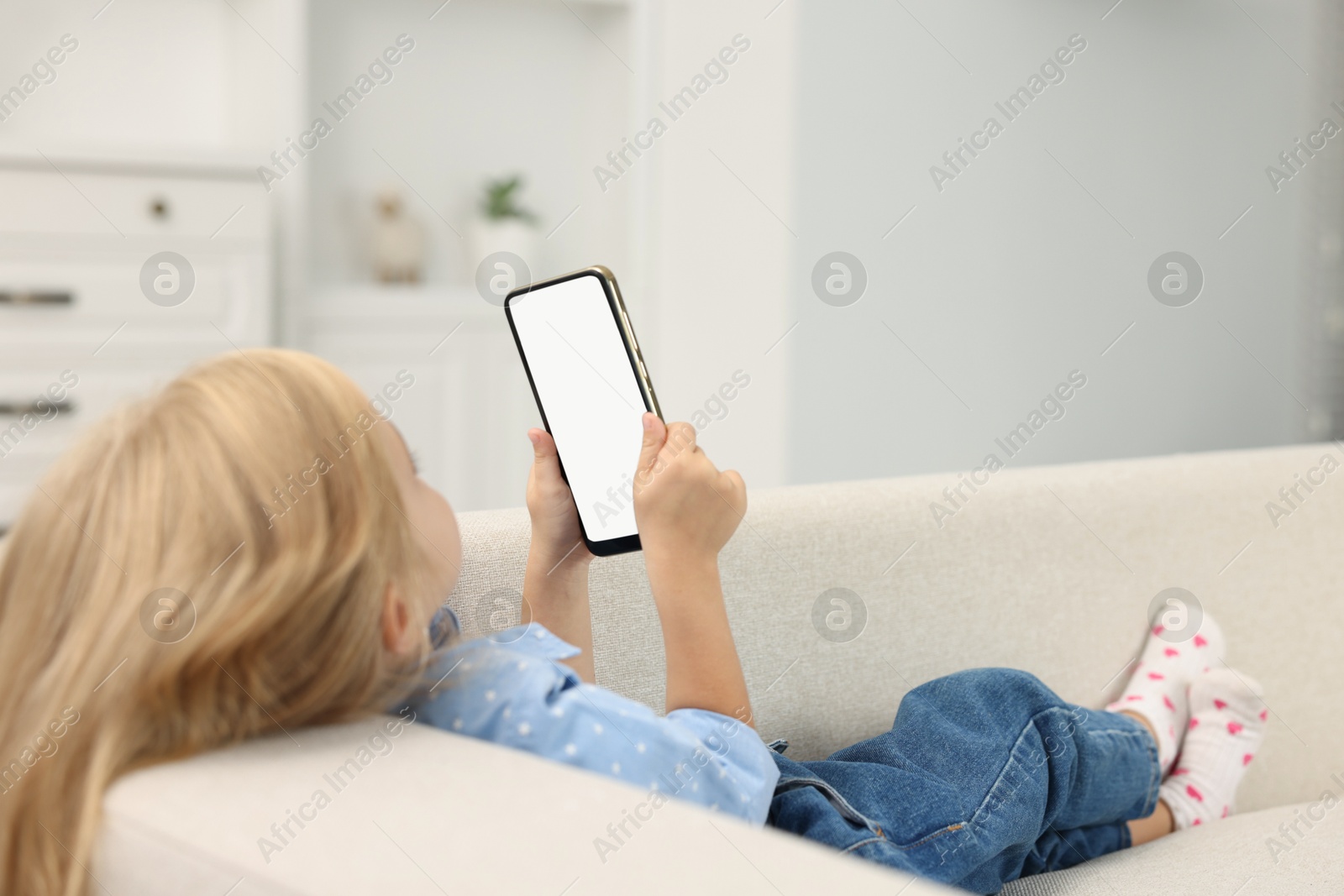 Photo of Cute little girl using smartphone on sofa at home