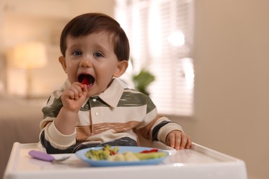 Photo of Cute little baby eating healthy food in high chair at home