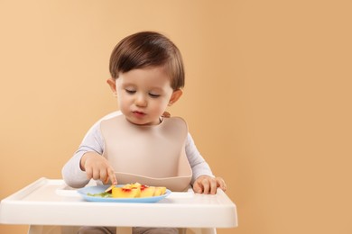 Photo of Healthy baby food. Cute little kid eating fruits in high chair on beige background