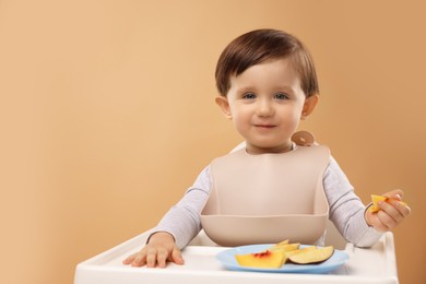 Photo of Healthy baby food. Cute little kid eating fruits in high chair on beige background