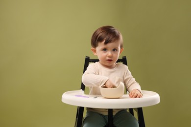 Photo of Cute little baby eating healthy food from bowl in high chair on olive background, space for text