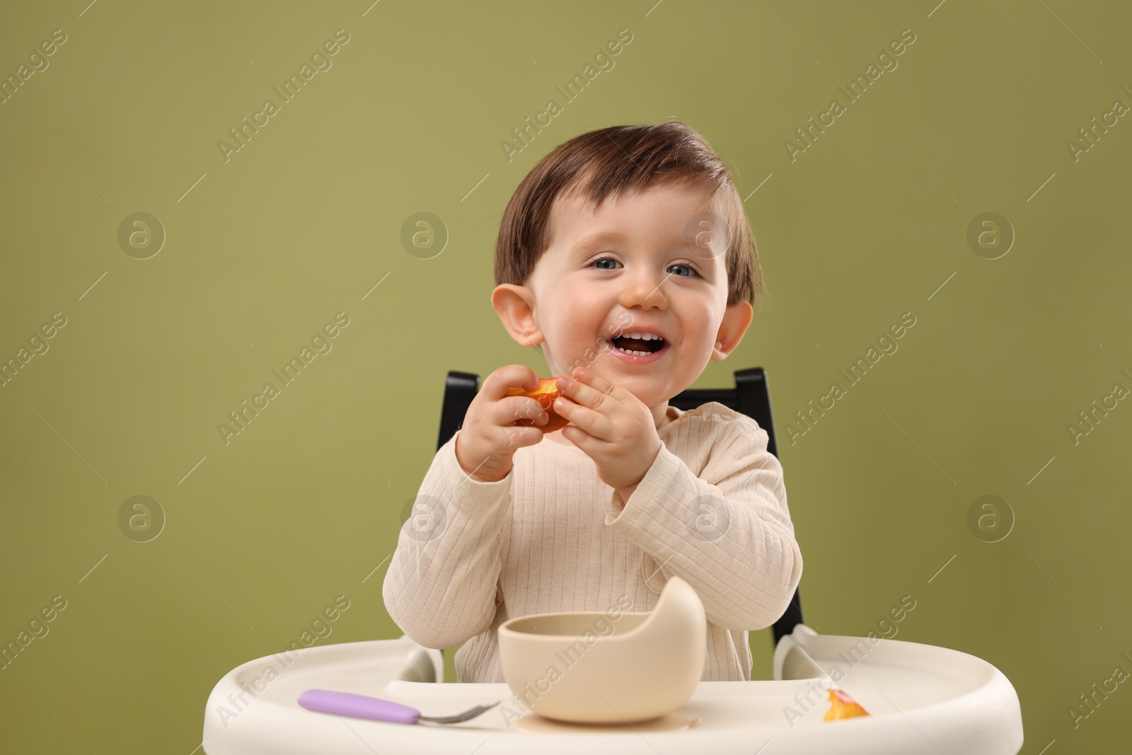 Photo of Cute little baby eating healthy food from bowl in high chair on olive background, space for text