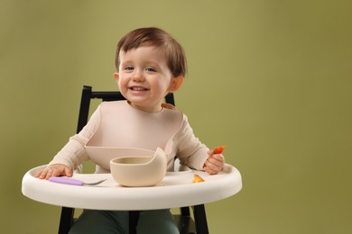 Photo of Cute little baby eating healthy food from bowl in high chair on olive background, space for text