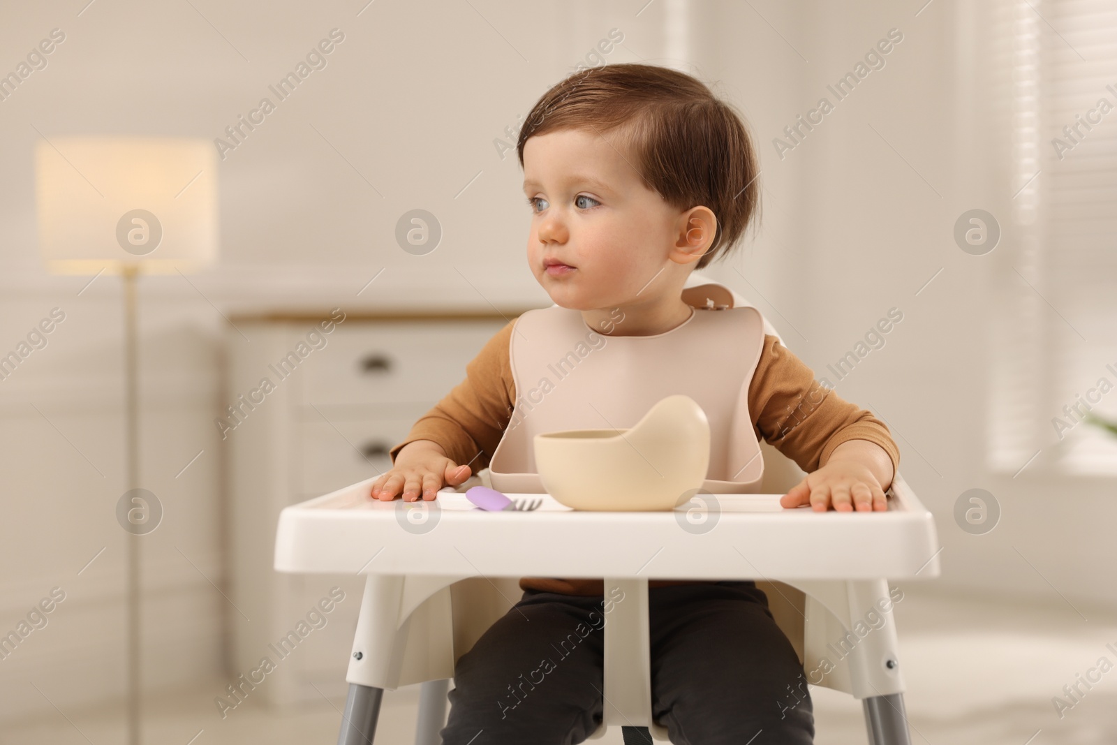 Photo of Cute little kid eating healthy baby food from bowl in high chair at home