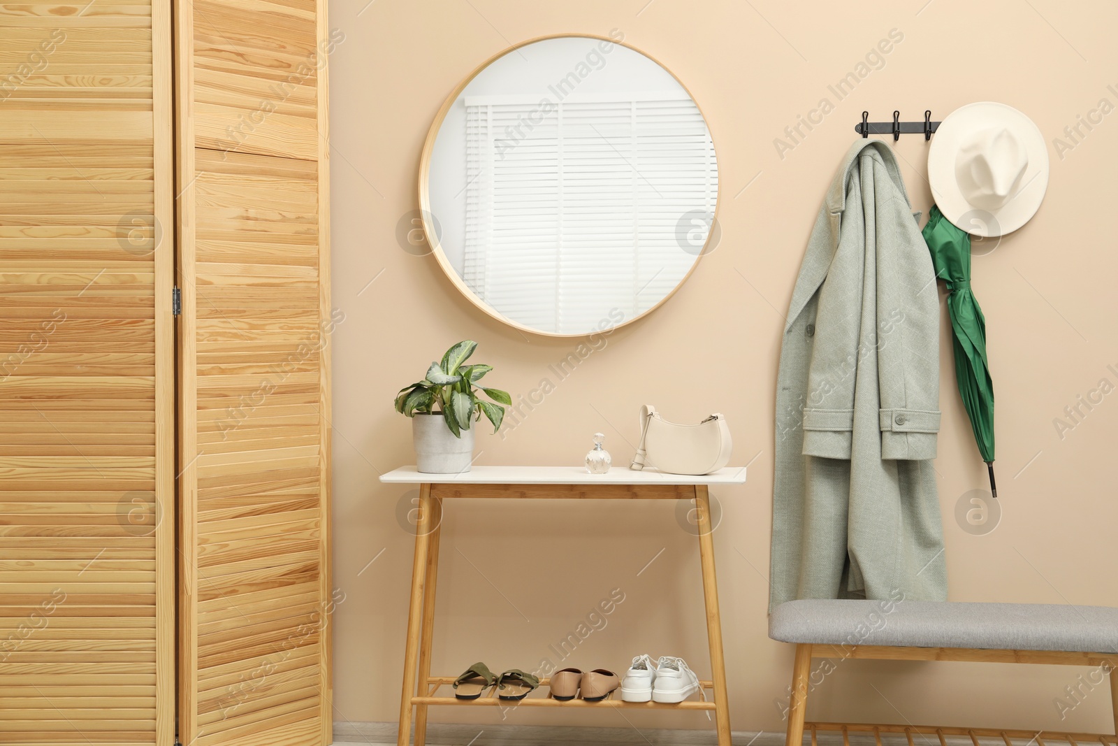 Photo of Coat rack with clothes, mirror, shoe storage benches and folding screen in hallway. Interior design