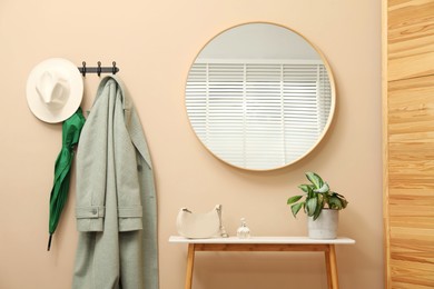 Photo of Coat rack with clothes, mirror and storage bench in hallway. Interior design