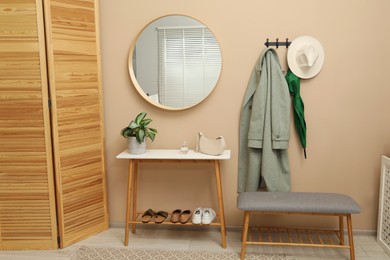 Photo of Coat rack with clothes, mirror, shoe storage benches and folding screen in hallway. Interior design