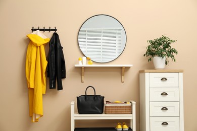 Coat rack with clothes, mirror, shoe storage bench and chest of drawers in hallway. Interior design