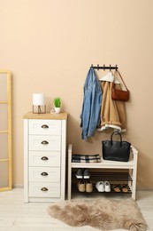 Coat rack with clothes, mirror, shoe storage bench and chest of drawers in hallway. Interior design