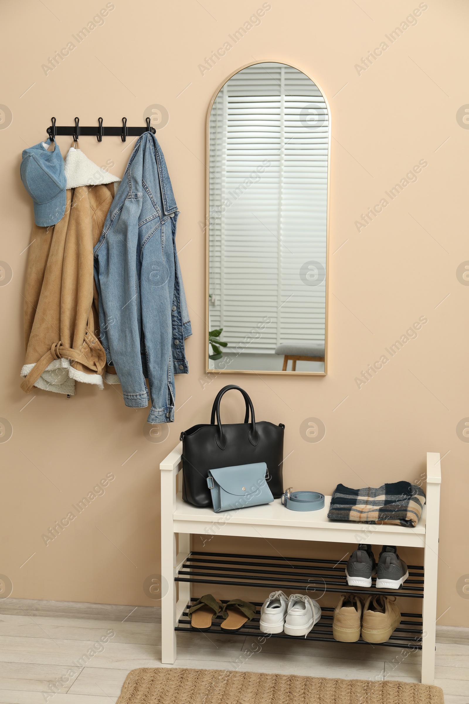 Photo of Coat rack with clothes, mirror and shoe storage bench in hallway. Interior design