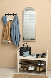 Photo of Coat rack with clothes, mirror and shoe storage bench in hallway. Interior design