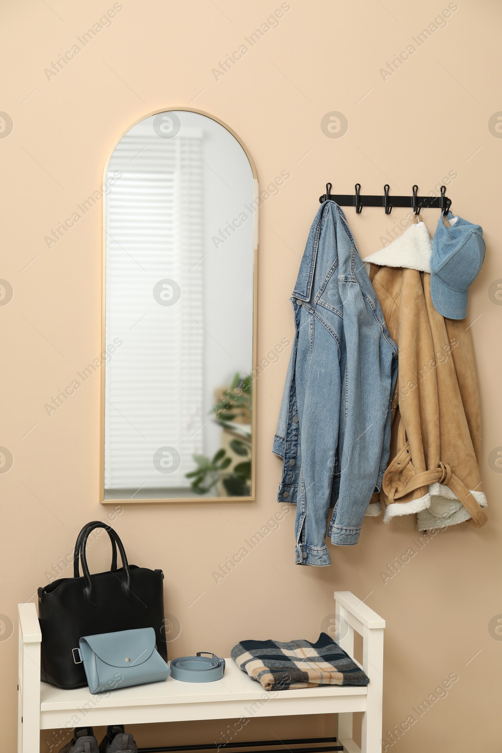 Photo of Coat rack with clothes, mirror and shoe storage bench in hallway. Interior design