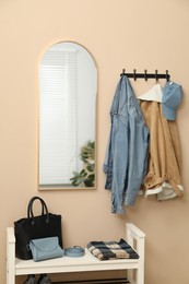 Photo of Coat rack with clothes, mirror and shoe storage bench in hallway. Interior design