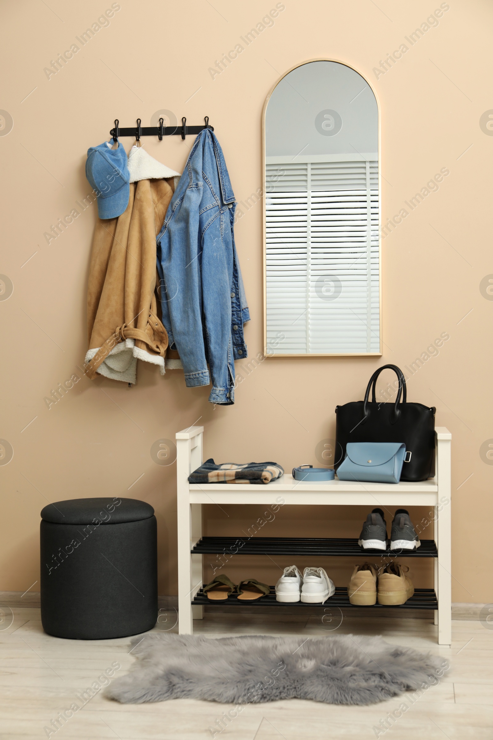 Photo of Coat rack with clothes, mirror, shoe storage bench and pouffe in hallway. Interior design