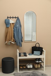 Photo of Coat rack with clothes, mirror, shoe storage bench and pouffe in hallway. Interior design