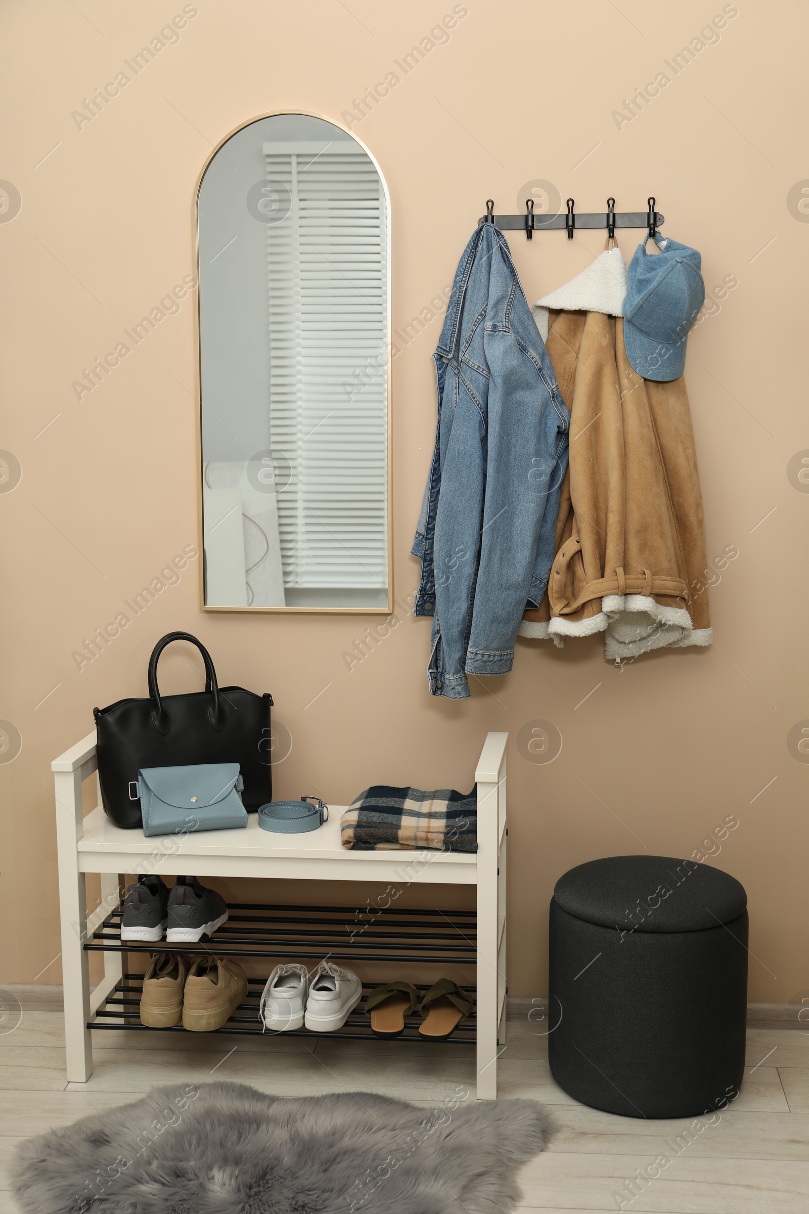 Photo of Coat rack with clothes, mirror, shoe storage bench and pouffe in hallway. Interior design