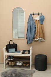 Coat rack with clothes, mirror, shoe storage bench and pouffe in hallway. Interior design