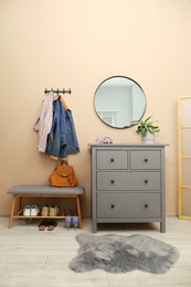 Photo of Coat rack with clothes, mirror, houseplant, shoe storage bench and chest of drawers in hallway. Interior design