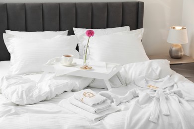 Photo of Breakfast tray, towels and bathrobe on bed with beautiful linens indoors