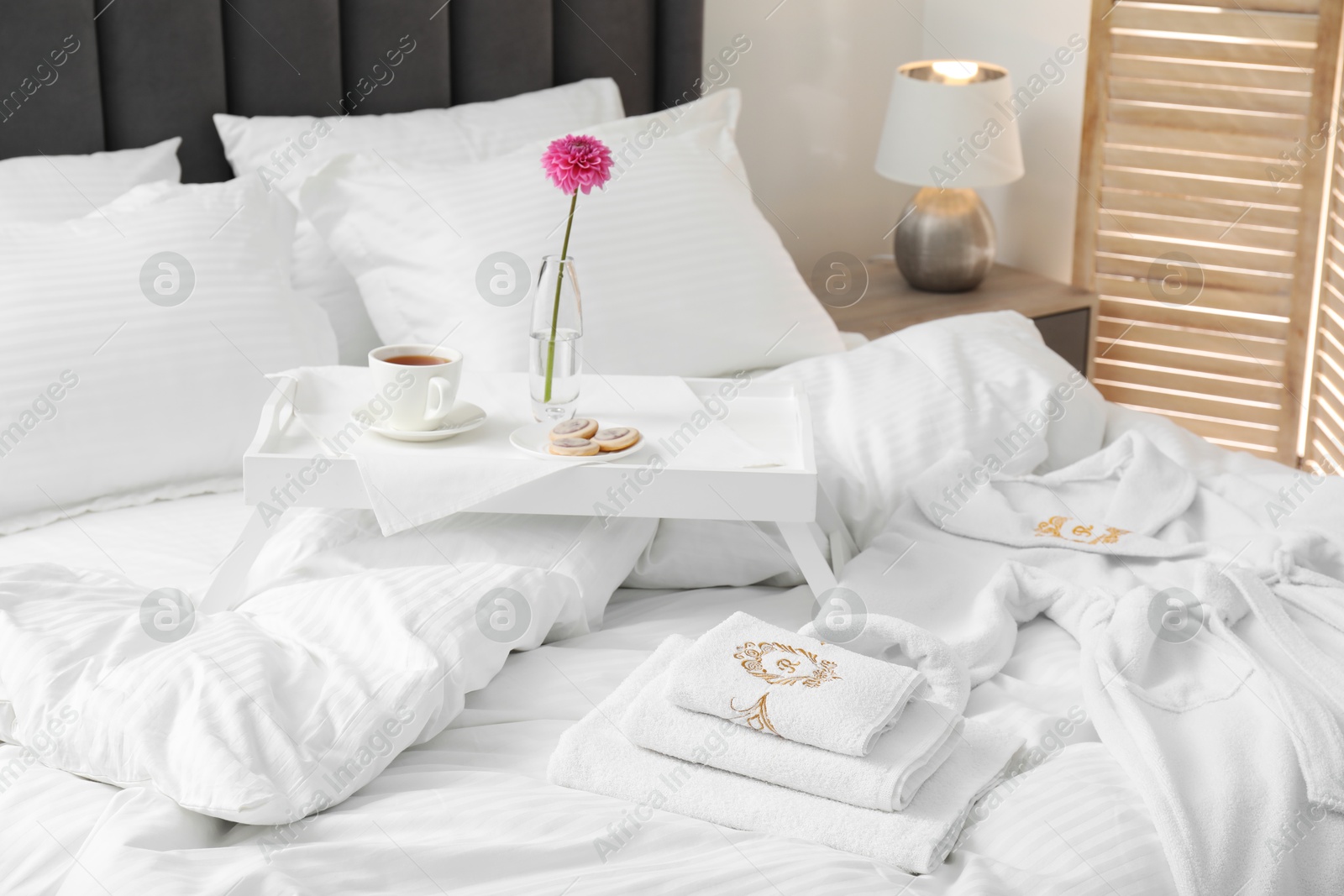 Photo of Breakfast tray, towels and bathrobe on bed with beautiful linens indoors