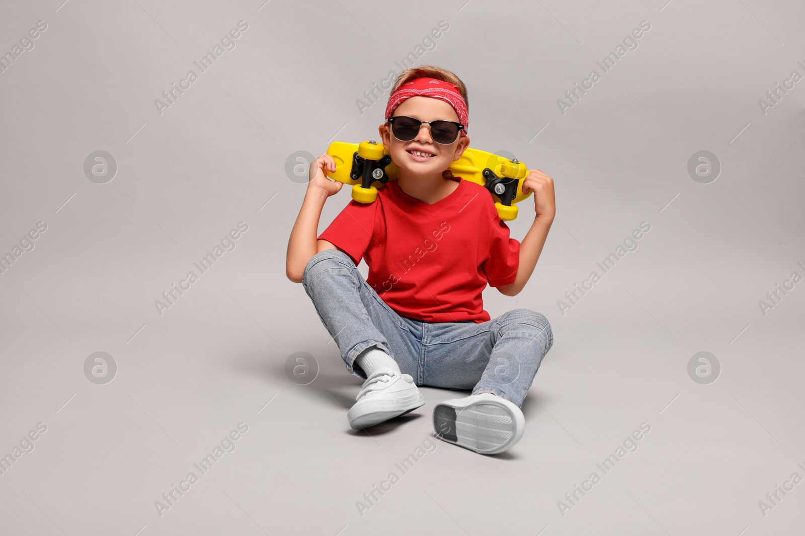 Photo of Little boy with sunglasses and skateboard on light grey background