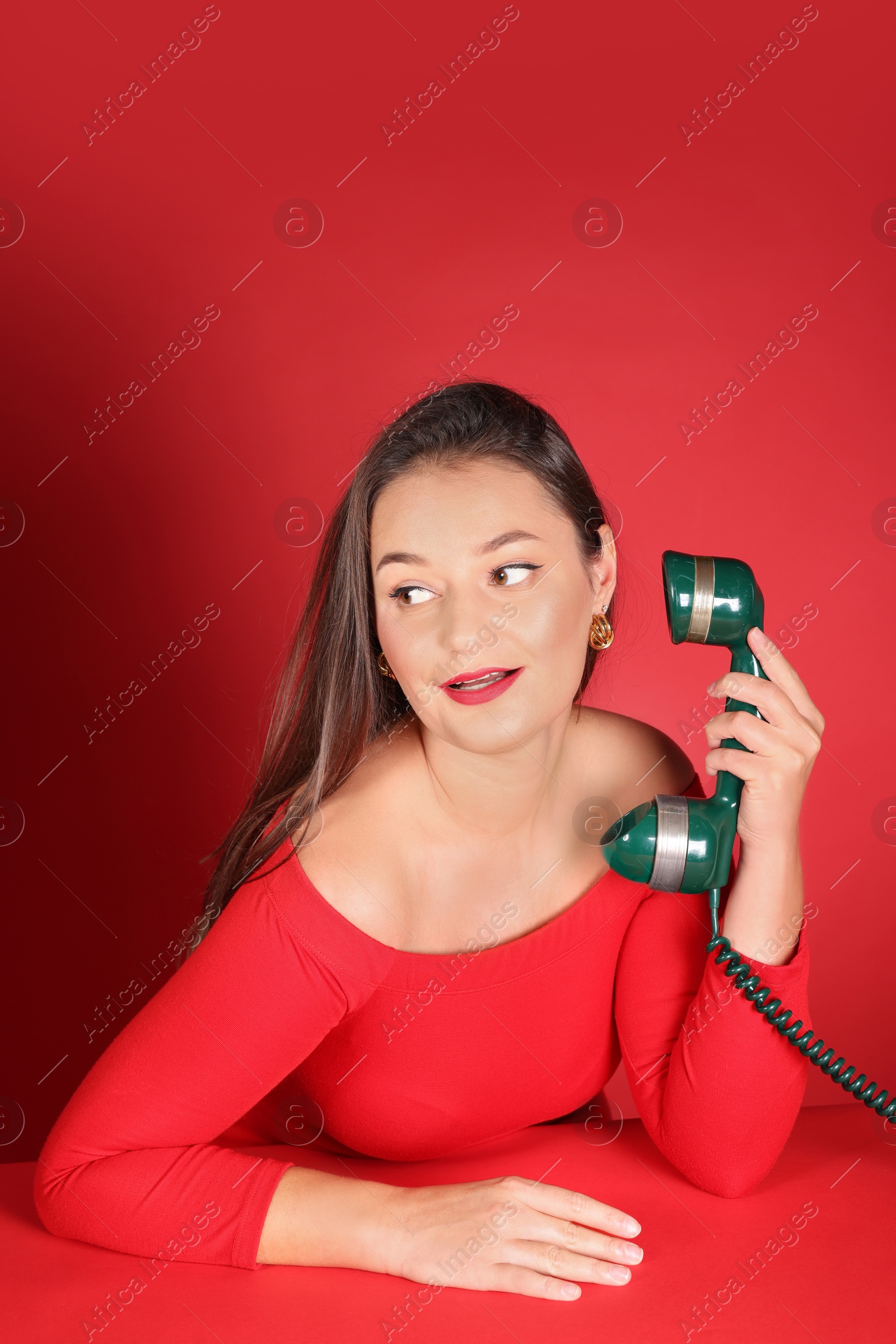 Photo of Woman talking on green vintage telephone against red background