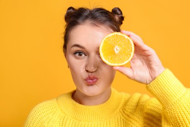 Photo of Happy girl holding orange half near eye on orange background