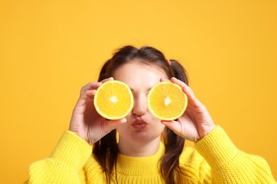 Photo of Happy girl holding orange halves near eyes on orange background