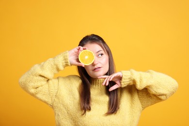 Photo of Young woman holding orange half near eye on orange background