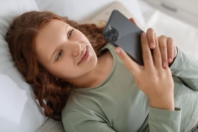 Photo of Beautiful teenage girl using smartphone on bed at home