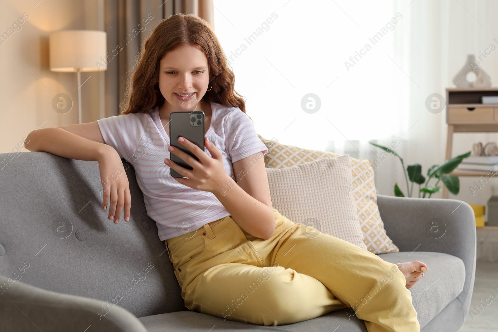 Photo of Beautiful teenage girl using smartphone on sofa at home