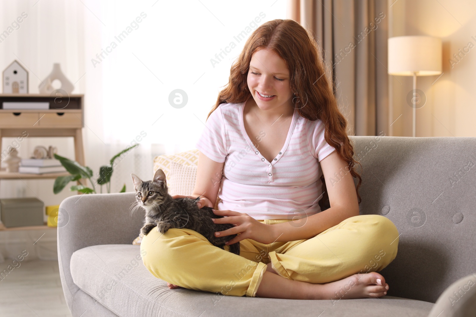 Photo of Beautiful teenage girl with cute cat on sofa at home