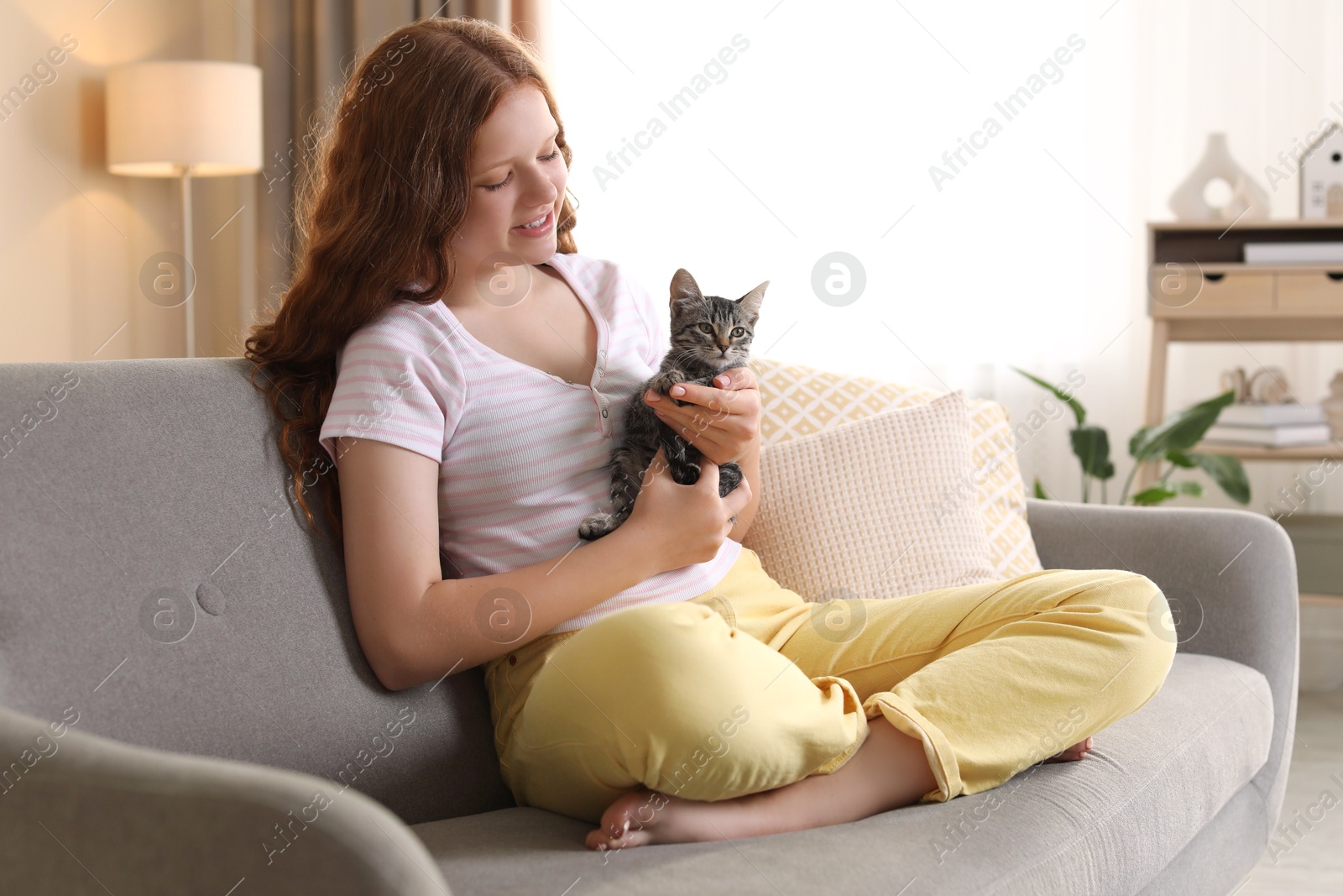 Photo of Beautiful teenage girl with cute cat on sofa at home