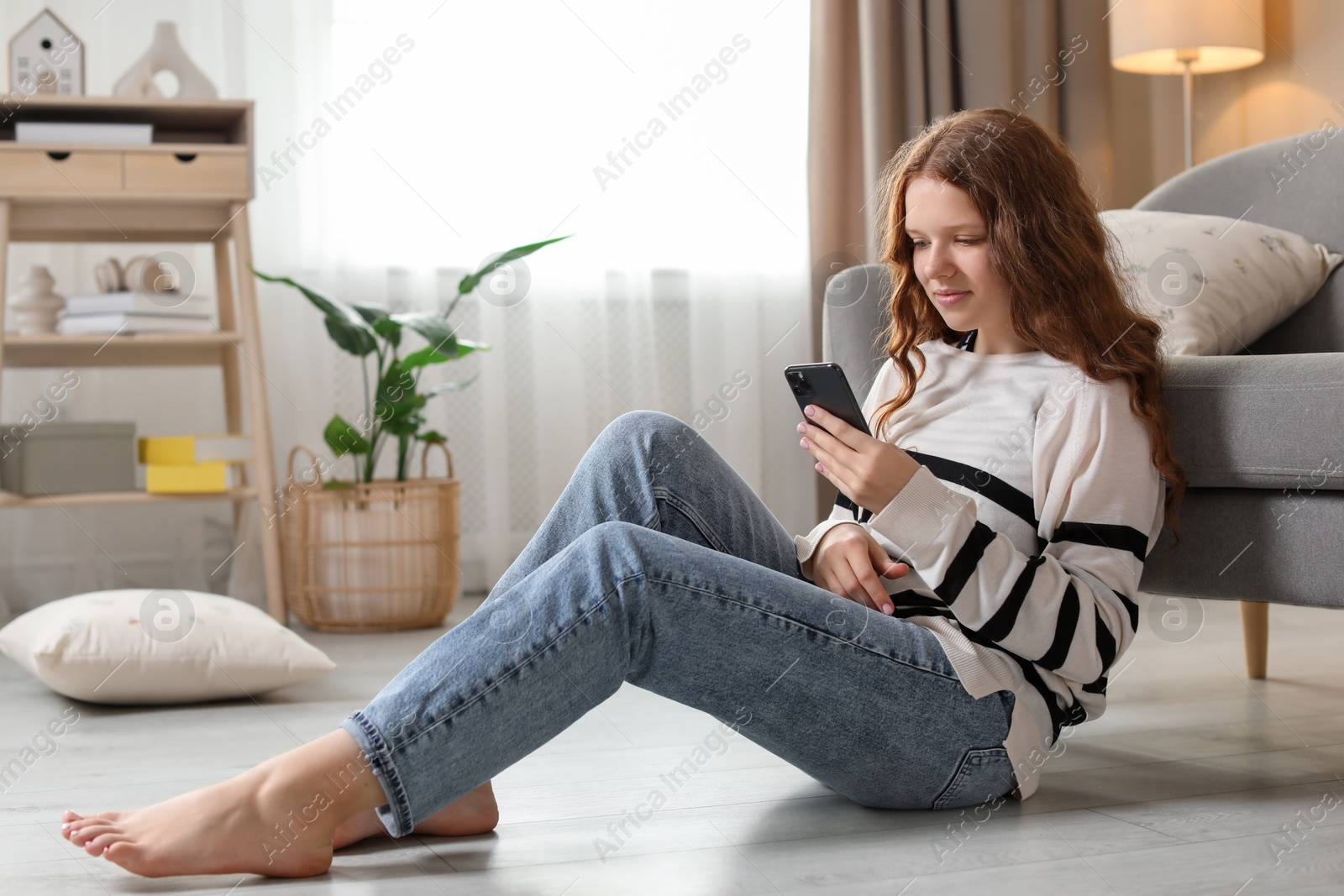 Photo of Beautiful teenage girl using smartphone on floor at home