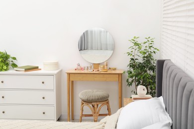 Photo of Mirror, dressing table, houseplant, bed and chest of drawers indoors. Interior design