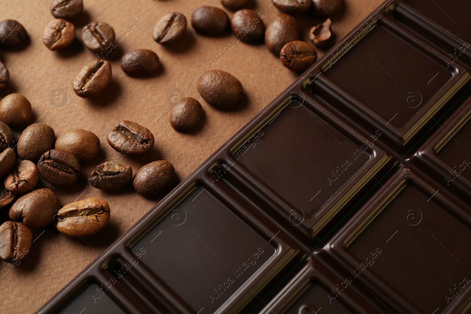 Photo of Tasty chocolate bar and coffee beans on brown background, closeup