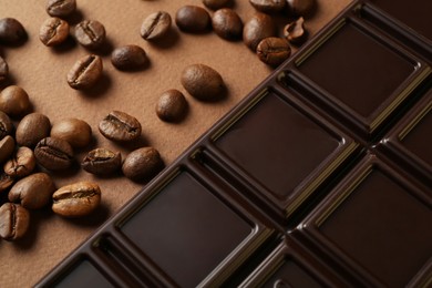 Tasty chocolate bar and coffee beans on brown background, closeup