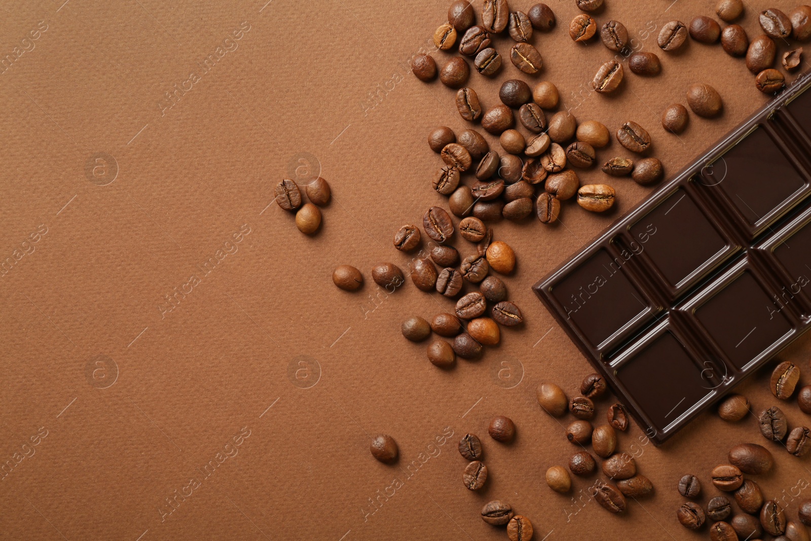 Photo of Tasty chocolate bar and coffee beans on brown background, top view. Space for text