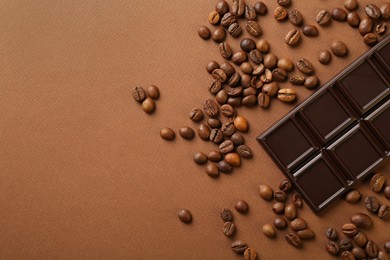 Photo of Tasty chocolate bar and coffee beans on brown background, top view. Space for text